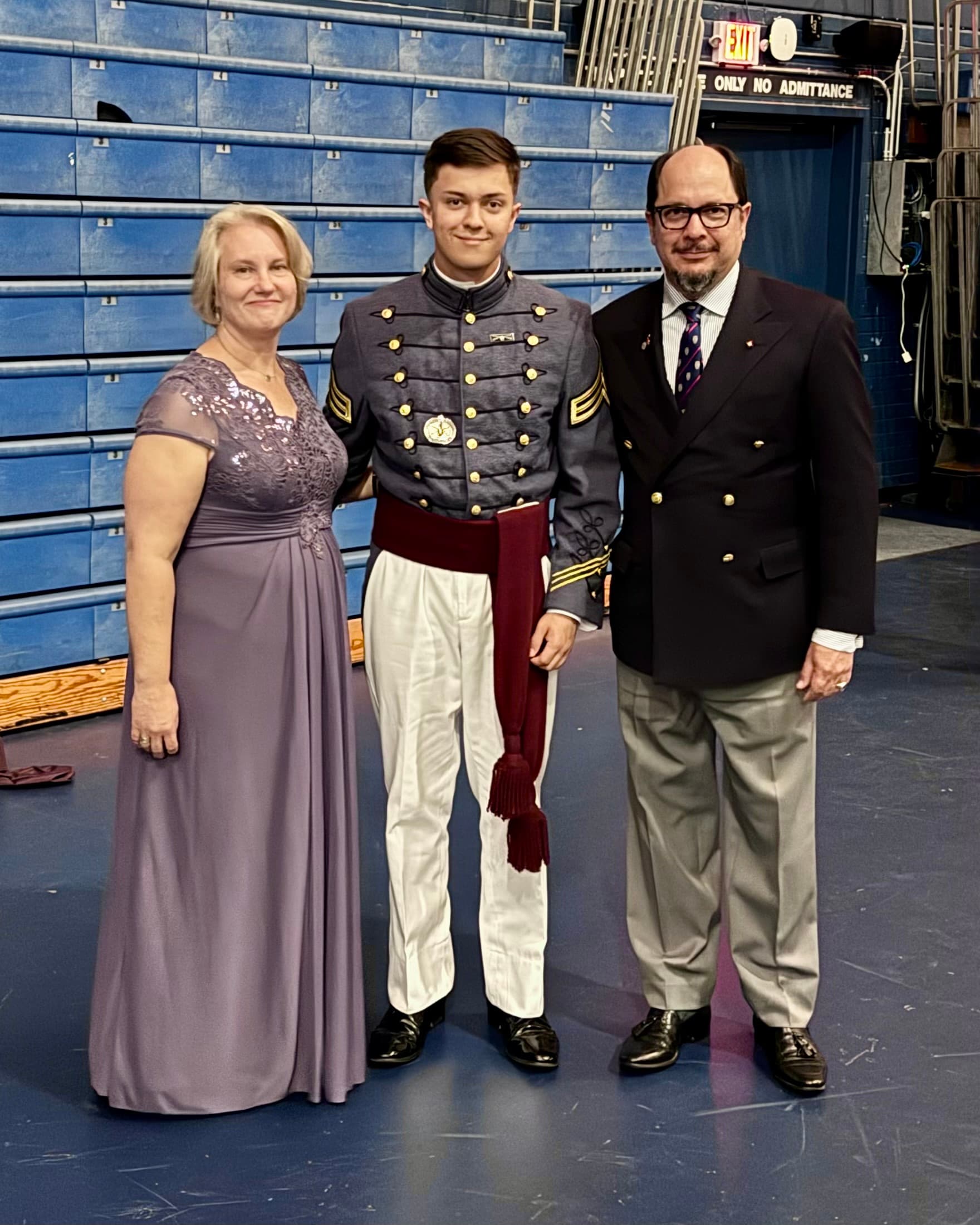 A cadet in dress uniform with the maroon class sash poses with family after the ring walk at McAlister Field House.