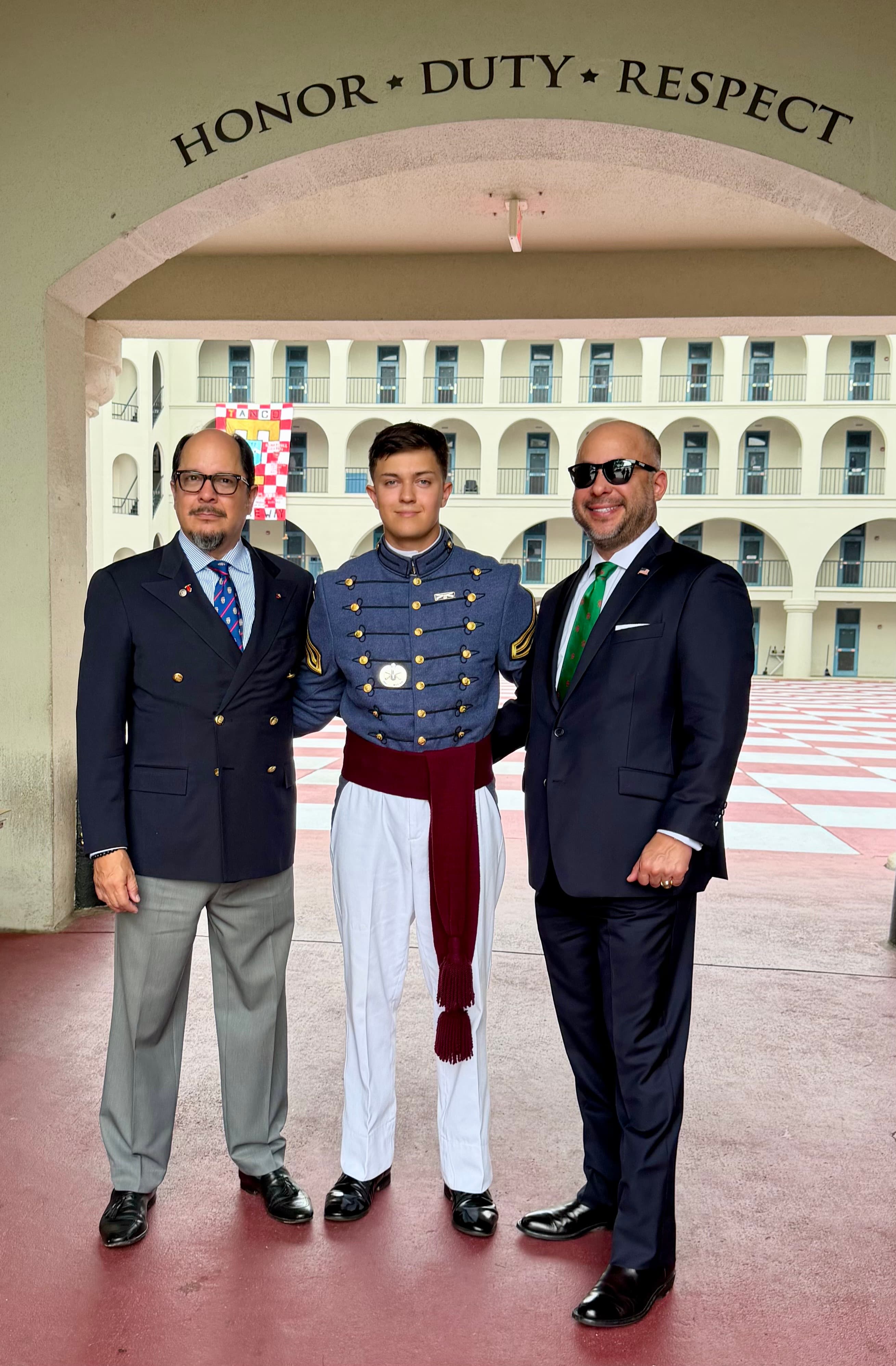 A cadet and family stand beneath the Honor Duty Respect arch at The Citadel barracks quad.