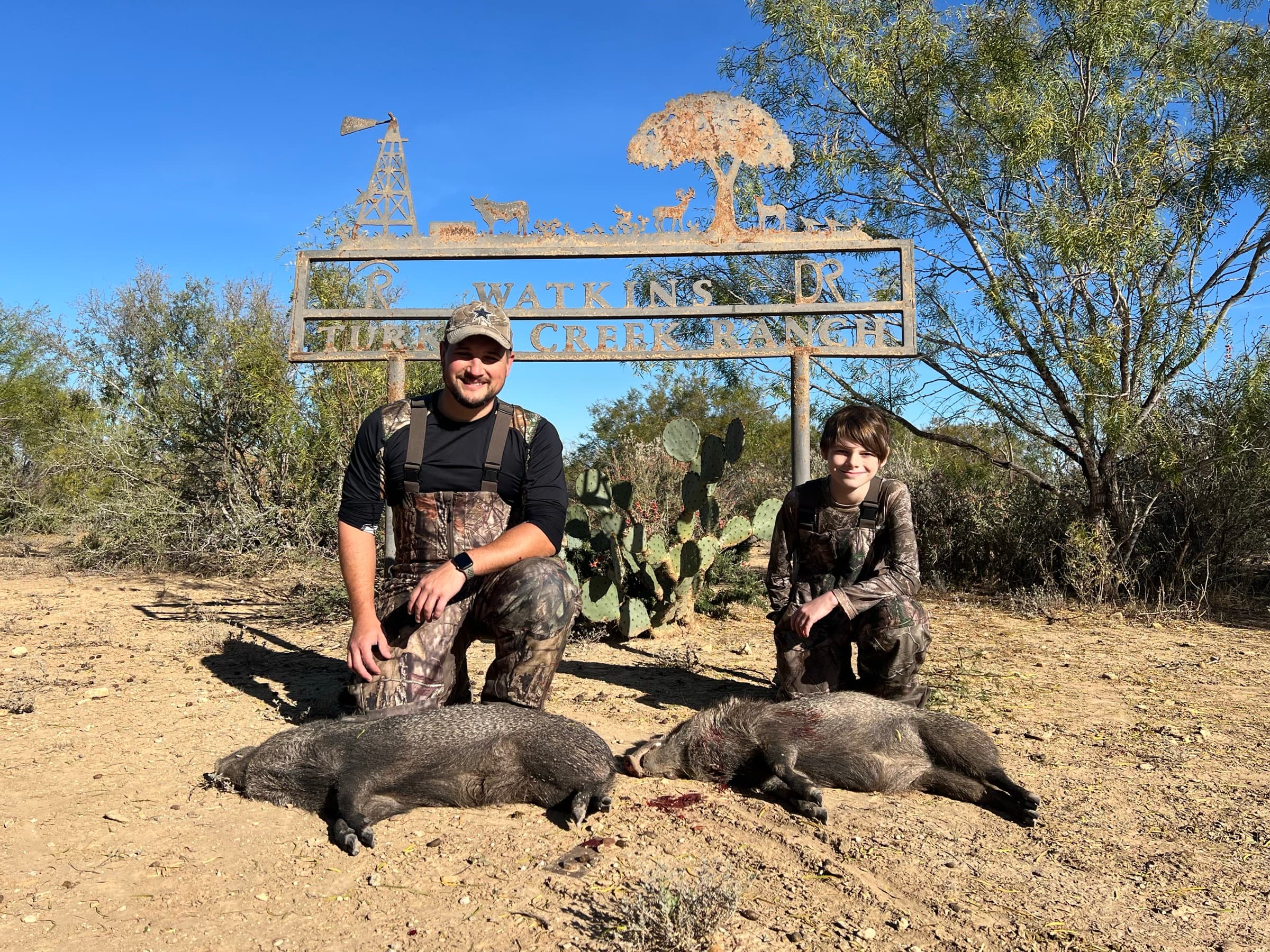 Two harvested wild hogs displayed at the base of the WS Turkey Creek Ranch entrance sign after a hunt.