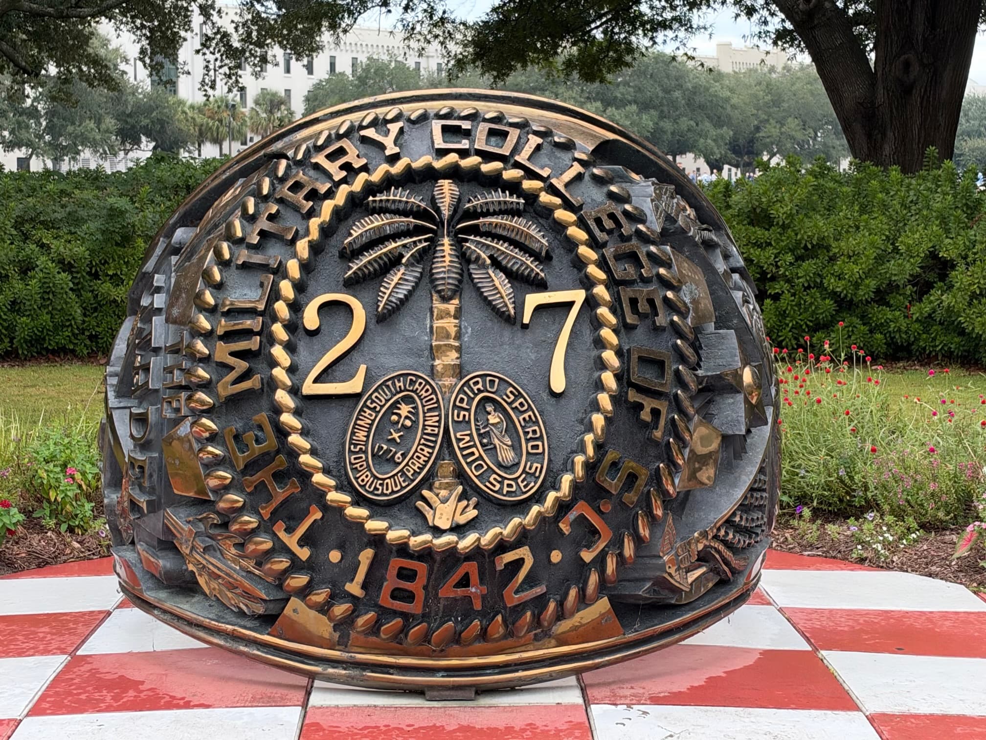 Bronze Class of 2027 ring sculpture on the checkered quad at The Citadel with the barracks beyond.