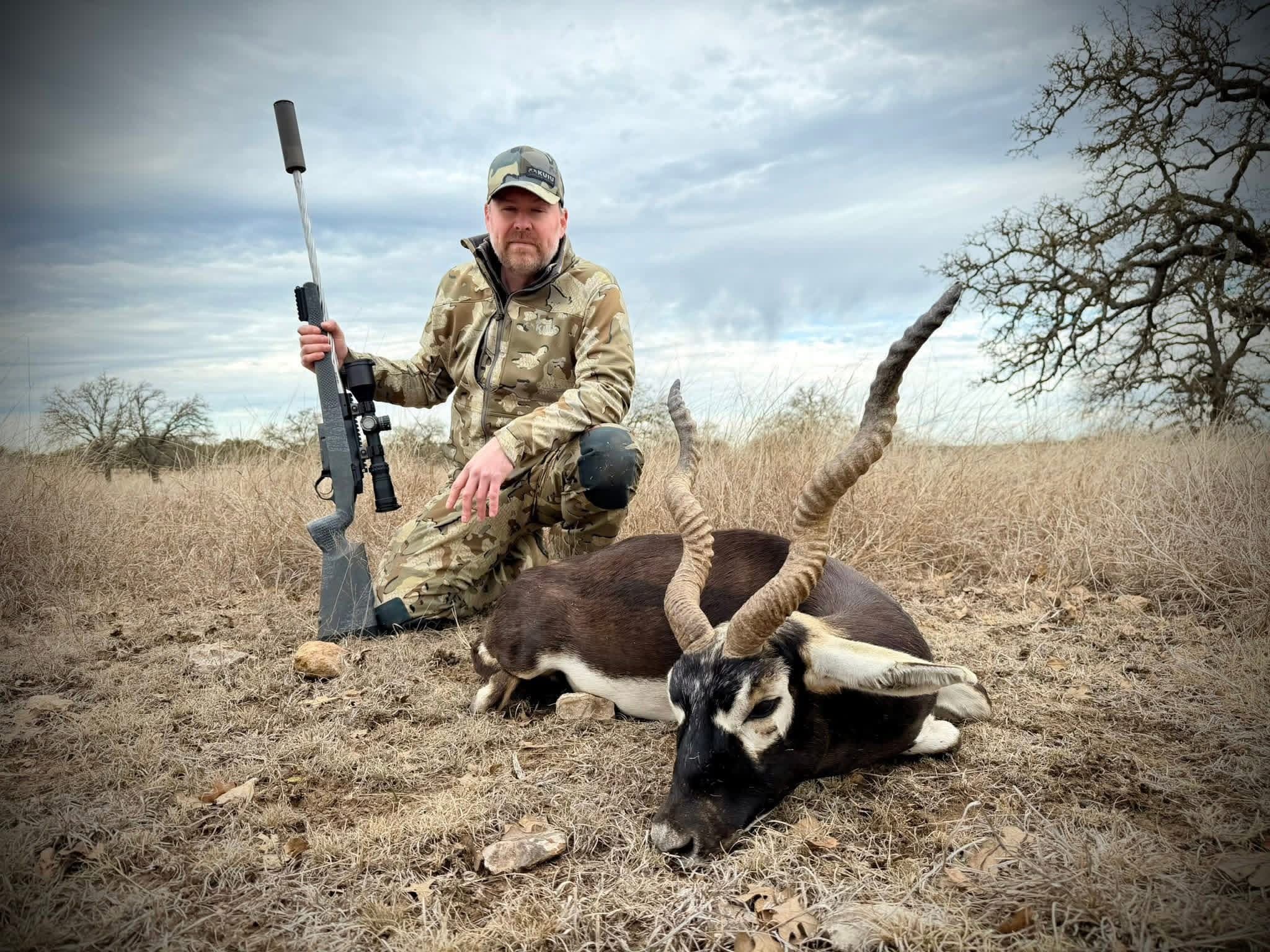 A hunter kneels behind a harvested blackbuck ram with a bolt-action rifle at Brochin Expeditions.