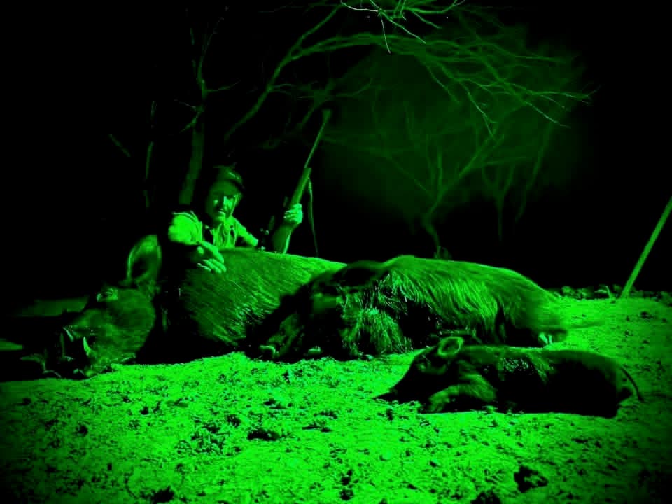 A night-vision image of a hunter beside two harvested wild hogs at Brochin Expeditions.