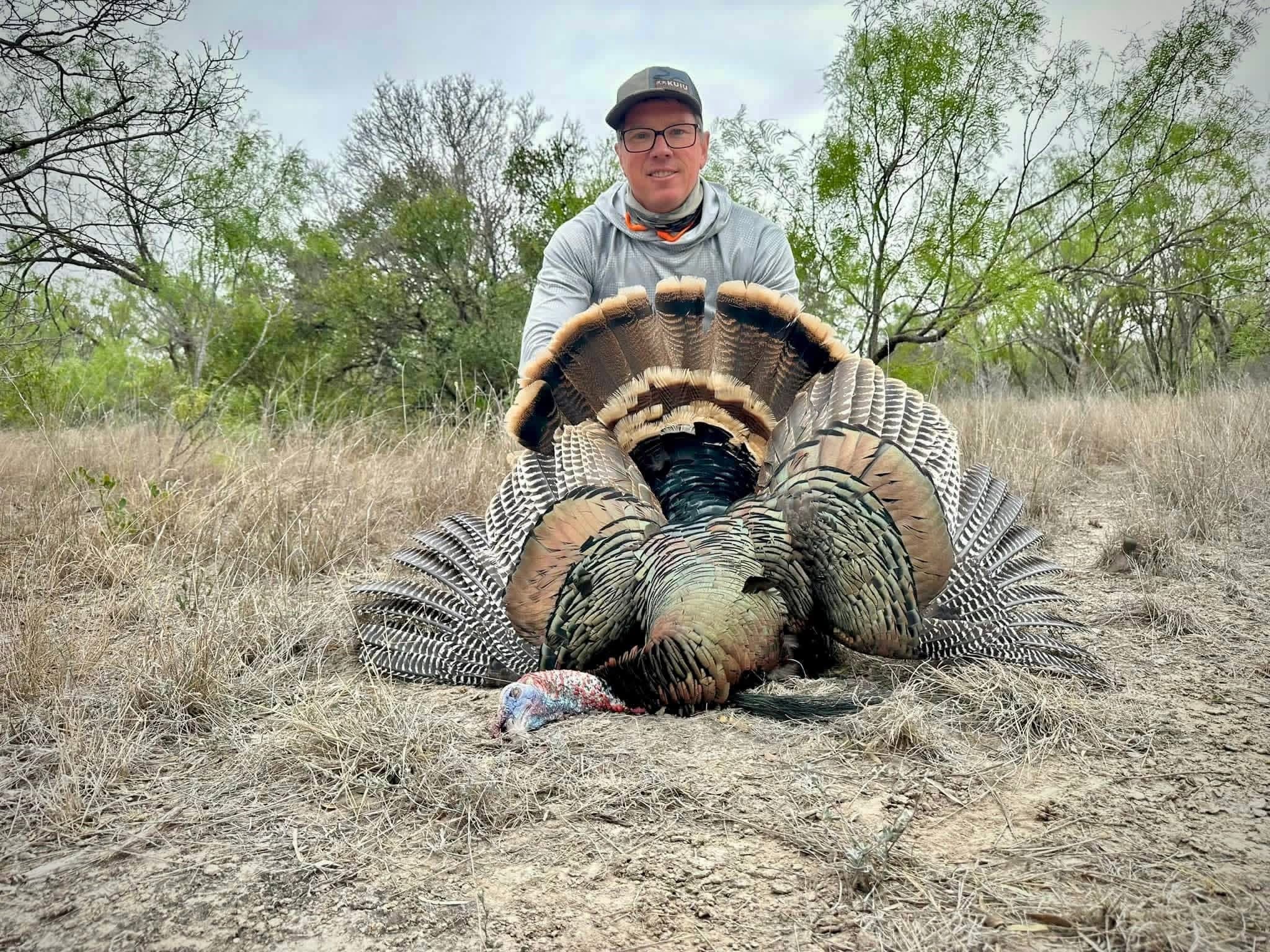 A hunter kneels behind a harvested wild turkey with its tail fanned at Brochin Expeditions.