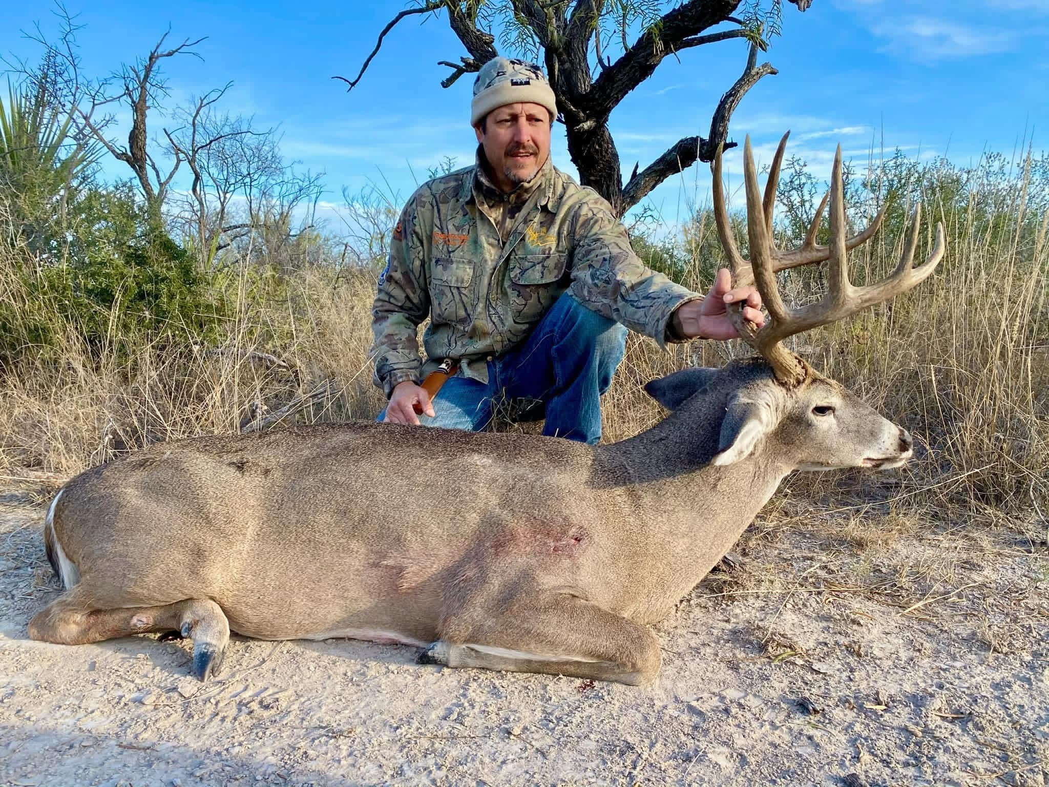 A hunter kneels behind a harvested whitetail buck in the South Texas brush country at Brochin Expeditions.