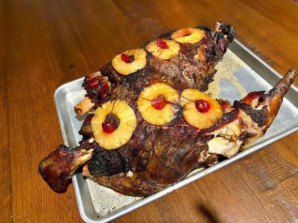 A roasted leg of lamb glazed with pineapple rings and cherries on a sheet pan at Brochin Expeditions.